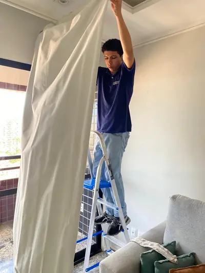 Técnico da PROLAVE sobre uma escada retirando a cortina da sala de um cliente para higienização